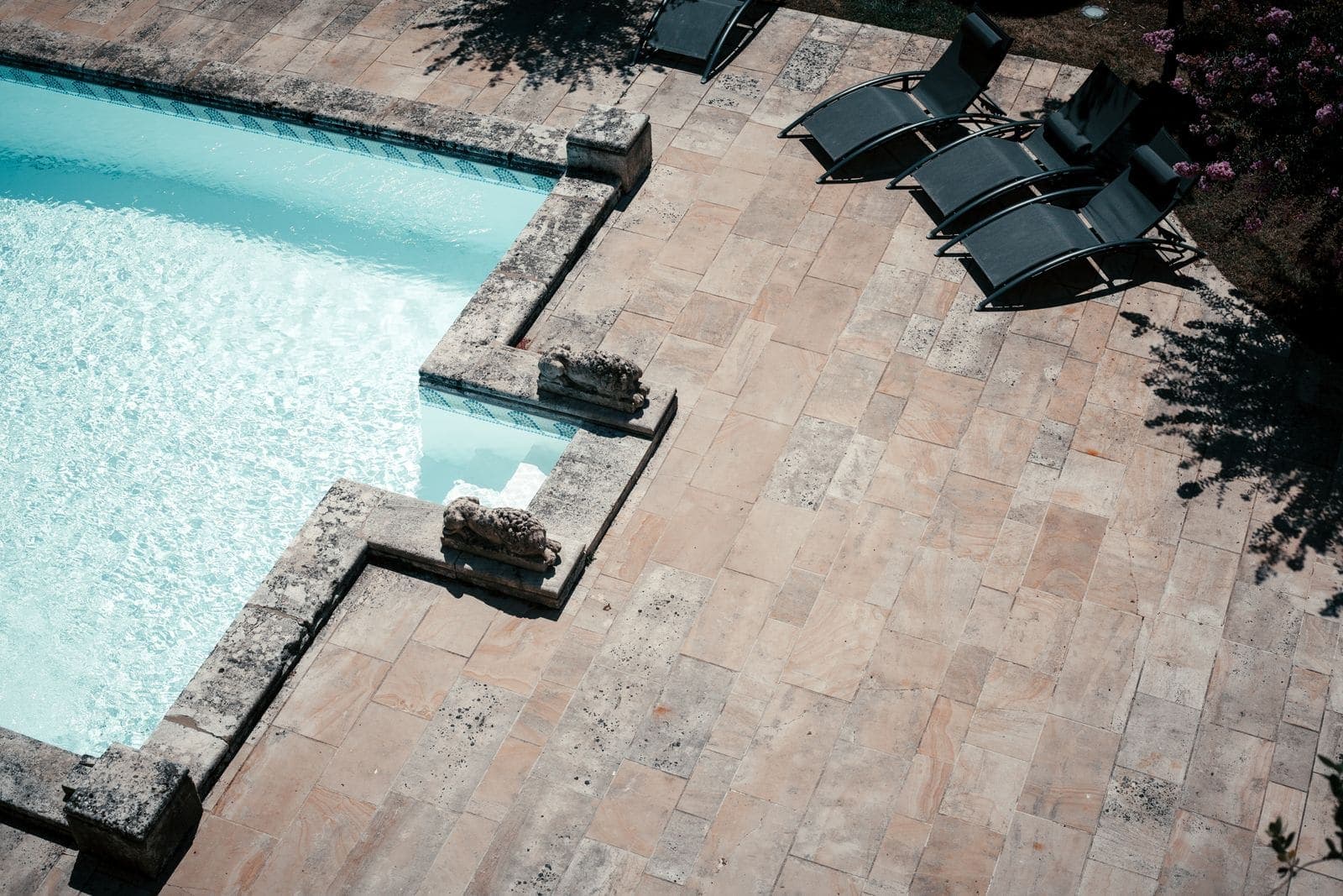 Travertine paver pool deck with lounge chairs at the edge of the water
