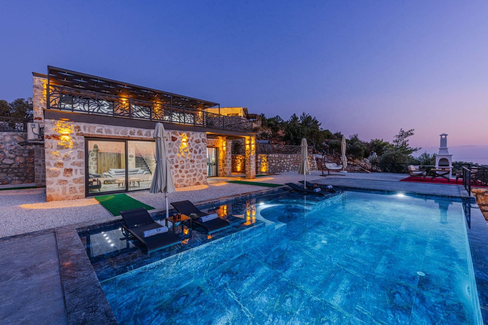 Custom shaped pool with a stone deck and landscape lighting at dusk