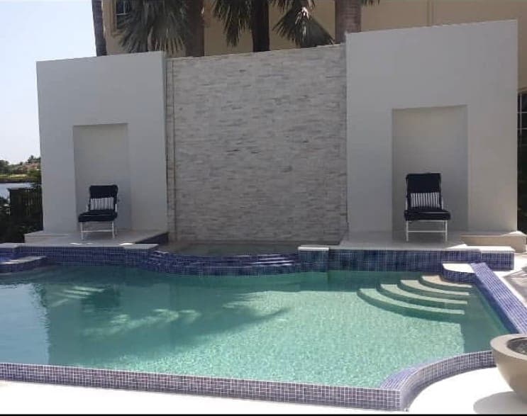 Gunite pool with a glass tile waterline, wide entry steps, and a white feature wall faced in stacked stone